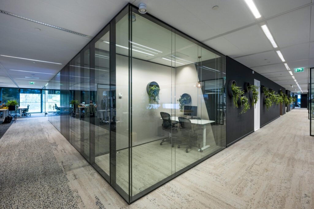Modern office hallway on Gustav Mahlerlaan with glass-walled meeting rooms and green wall-mounted plant decor.